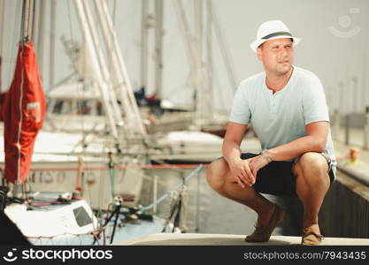 Handsome fashion man tourist on pier in port with yachts. Guy enjoying summer travel vacation by sea.