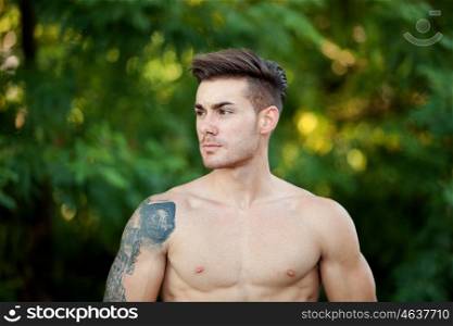 Handsome fit athletic shirtless young man against green nature