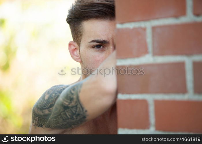 Handsome fit athletic shirtless young man with a tattoo leaning against a brick wall