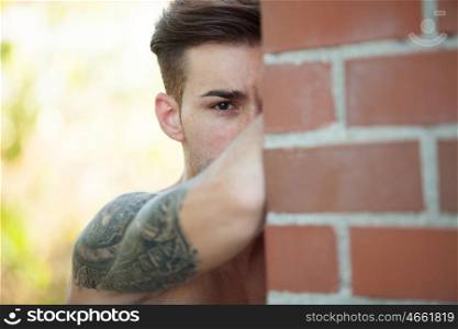 Handsome fit athletic shirtless young man with a tattoo leaning against a brick wall
