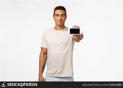 Handsome good-looking strong athletic man in t-shirt, stretch hand, holding smartphone horizontally, promote app or new mobile game, smiling assertive, advice download something, advertise store.. Handsome good-looking strong athletic man in t-shirt, stretch hand, holding smartphone horizontally, promote app or new mobile game, smiling assertive, advice download something, advertise store