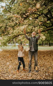 Handsome grandfather spending time with his granddaughter in park on autumn day