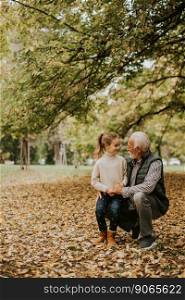 Handsome grandfather spending time with his granddaughter in park on autumn day