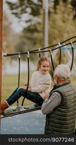 Handsome grandfather spending time with his granddaughter in park playground on autumn day