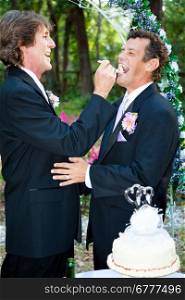 Handsome groom feeds his new husband wedding cake at their reception.
