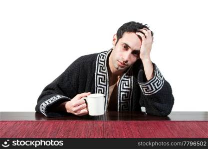 Handsome guy in the morning who just woke up sitting at a table in his robe with a cup recovering from his hangover, isolated on white