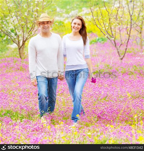 Handsome guy wearing hat and cute girl holding pink flowers bouquet walking in spring park, romantic feelings, love concept