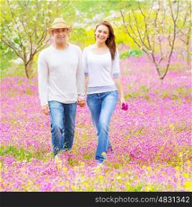 Handsome guy wearing hat and cute girl holding pink flowers bouquet walking in spring park, romantic feelings, love concept