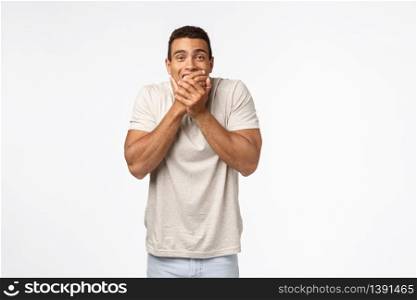 Handsome happy young hispanic muscline guy in t-shirt, laughing and covering smiling mouth as trying keep silent, chuckling inside, standing amused watching hilarious scene, white background.. Handsome happy young hispanic muscline guy in t-shirt, laughing and covering smiling mouth as trying keep silent, chuckling inside, standing amused watching hilarious scene, white background