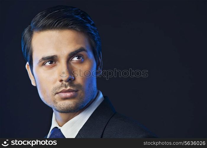Handsome Indian businessman looking away over black background