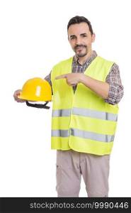 Handsome male contractor in reflective vest standing on white background and pointing at protective yellow hardhat while looking at camera. Builder with hardhat in studio