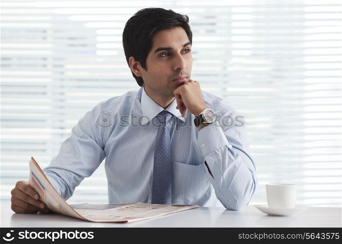 Handsome male executive in deep thought with newspaper at office