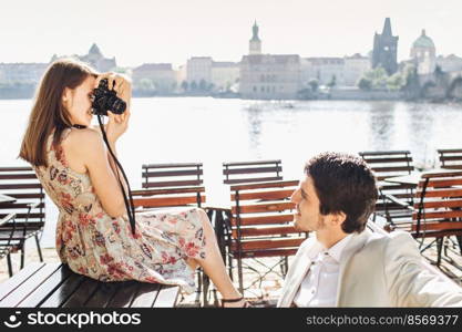 Handsome male poses at camera, being in good mood, spends free time with girlfriend who photographs him, wonderful landscape in background. Female and male active tourists go sightseeing together