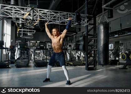 Handsome male weightlifter with ideal body training at modern sport gym. Young shirtless sportsman bodybuilder pushing barbell up doing exhale. Handsome male weightlifter with ideal body training at modern sport gym
