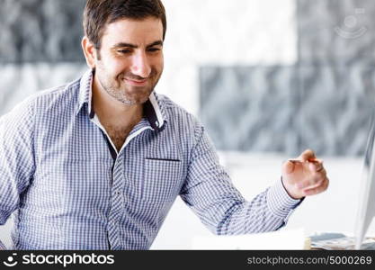 Handsome male worker in office. Handsome young businessman in office sitting at desk