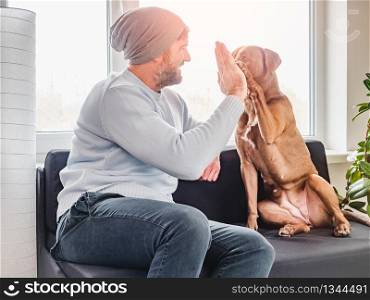 Handsome man and a charming puppy. Close-up, indoors. Studio photo, white color. Concept of care, education, obedience training and raising pets. Handsome man and a charming puppy. Close-up