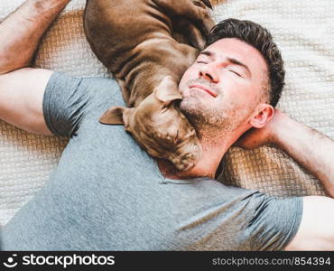 Handsome man and young, charming puppy, resting on a plaid. Close-up, white isolated background. Studio photo. Concept of care, education, training and raising of animals. Man and charming puppy resting on a plaid