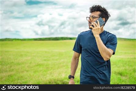 Handsome man calling on the phone in the field. man on the road talking on the phone, person in the field calling on the phone, young man talking on the phone in the field looking to the side