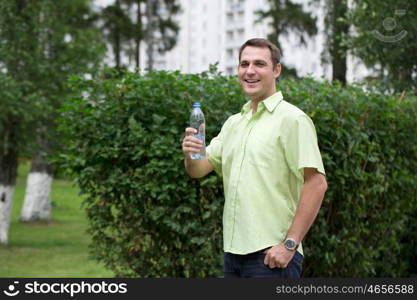 Handsome man drinking water in summer park