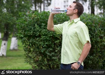 Handsome man drinking water in summer park