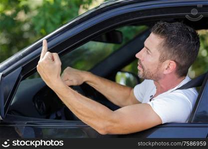 handsome man driving a car and showing the middle finger
