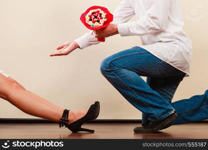 Handsome man giving woman candy bunch flowers. Young boyfriend with present gift kneeling in front of girlfriend. loving couple. Love.