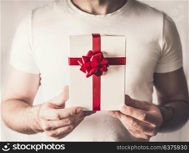 Handsome man holding gift box in hands with red ribbon , close up. Valentines day concept