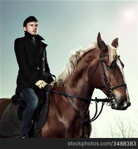 Handsome man in a black coat riding on a brown horse
