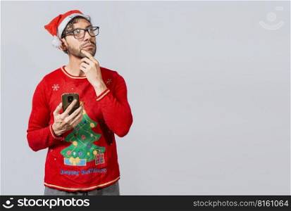 Handsome man in christmas clothes thoughtful holding cell phone. Thoughtful man with christmas hat holding cell phone, Young man in christmas clothes thoughtful with cell phone isolated