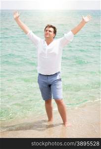Handsome man in white shirt enjoying sea and raising hands in the sky