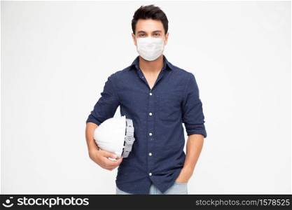 Handsome man industrial engineer holding a white helmet and wearing protective medical mask for prevent virus Covid-19 and looking at camera isolated on white background