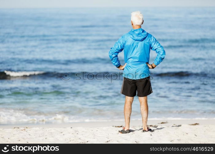Handsome man looking thoughtful while standing alone on beach. Handsome man looking thoughtful while standing alone on beach in sports wear