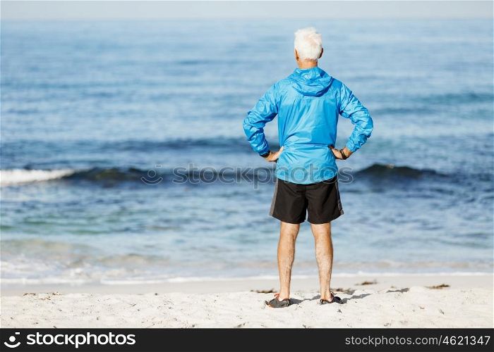 Handsome man looking thoughtful while standing alone on beach. Handsome man looking thoughtful while standing alone on beach in sports wear