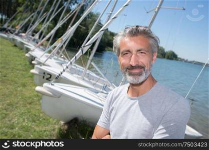 handsome man posing in front of sailing boats and lake