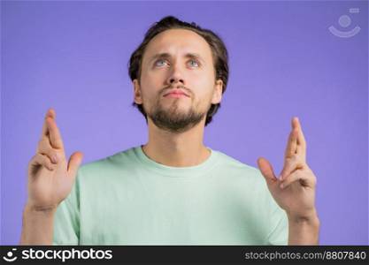 Handsome man praying with crossed fingers over violet background. Guy begging someone satisfy his desires, help with. Handsome man praying with crossed fingers over violet background. Guy begging someone satisfy his desires, help with.