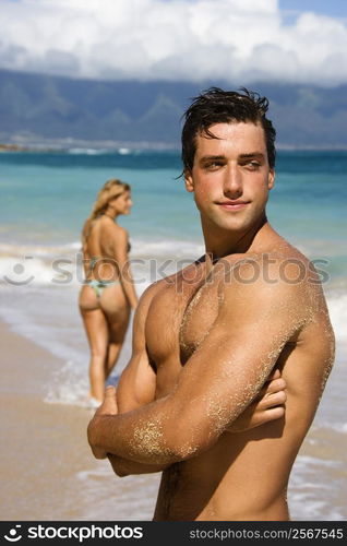 Handsome man standing on Maui, Hawaii beach with woman in background.