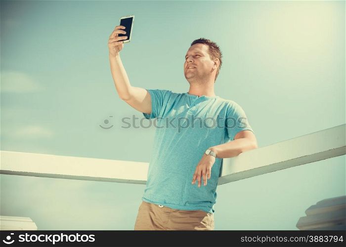 Handsome man tourist on pier taking selfie with smartphone. Fashion guy enjoying summer travel vacation by sea. Relax and technology concept.. Man tourist on pier taking selfie with smartphone.