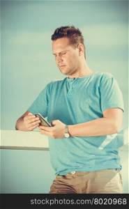 Handsome man tourist on pier using smartphone. Fashion guy enjoying summer travel vacation by sea. Relax and technology concept.. Man tourist on pier using smartphone. Technology.