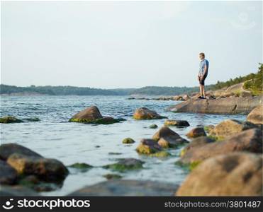 Handsome man walking on the rocky shore, beautiful summer evening