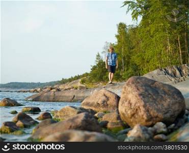 Handsome man walking on the rocky shore, beautiful summer evening