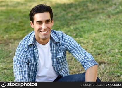 Handsome man wearing casual clothes sitting on grass of an urban park.