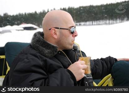 Handsome man wearing sunglasses relaxing and having coffee on a winter day.