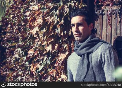 Handsome man wearing winter clothes in autumn leaves background. Young male with swater and scarf.