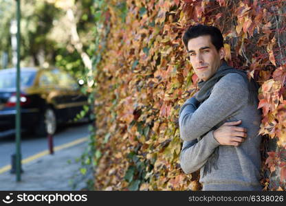 Handsome man wearing winter clothes in autumn leaves background. Young male with swater and scarf.