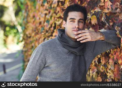 Handsome man wearing winter clothes in autumn leaves background. Young male with swater and scarf.