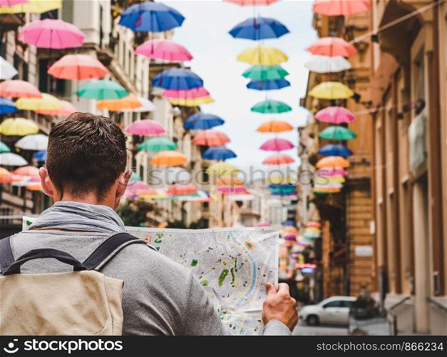 Handsome man with a tourist map on the background of a beautiful street of the fabulous city of Genoa on a cloudy, rainy day. Travel and vacation concept. Handsome man with a tourist map on a cloudy day