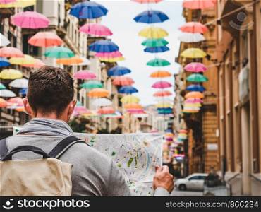 Handsome man with a tourist map on the background of a beautiful street of the fabulous city of Genoa on a cloudy, rainy day. Travel and vacation concept. Handsome man with a tourist map on a cloudy day