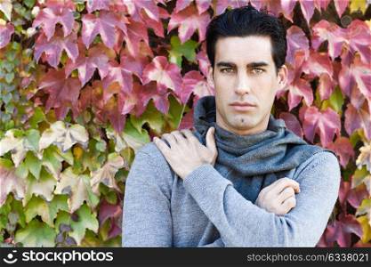 Handsome man with blue eyes wearing winter clothes in autumn leaves background. Young male with swater and scarf.
