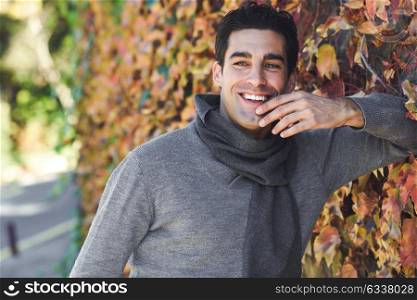 Handsome man with blue eyes wearing winter clothes smiling in autumn leaves background. Young male with swater and scarf.