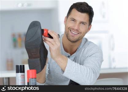 handsome man with brush cleaning black leather shoe